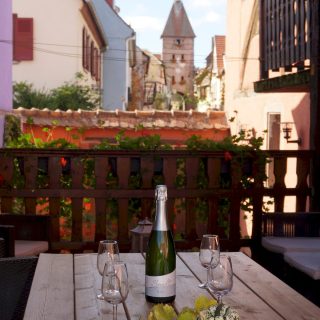 Terrasse, table à manger, vue sur l'entrée Ouest d'Ammerschwihr, la Porte Haute ''Obertor'' surmontée d'un nid de Cigogne blanche.